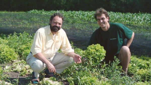 KI generiert: Zwei Personen knien in einem Salatfeld und lächeln in die Kamera.