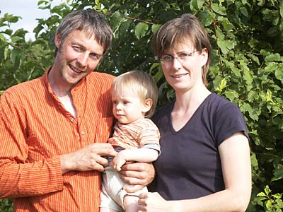 KI generiert: Ein Mann und eine Frau mit einem Kind auf dem Arm stehen draußen vor grünen Blättern.