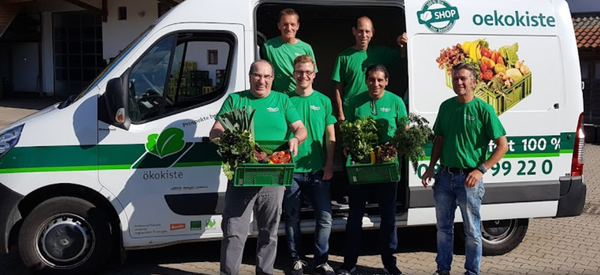 KI generiert: Fünf Männer in grünen T-Shirts mit Gemüsekisten vor einem Lieferwagen mit "oeko-kiste"-Logo.
