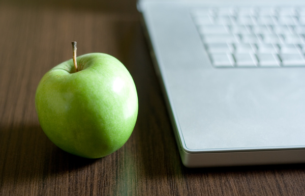 KI generiert: Ein grüner Apfel neben einem Laptop auf einem Holztisch.