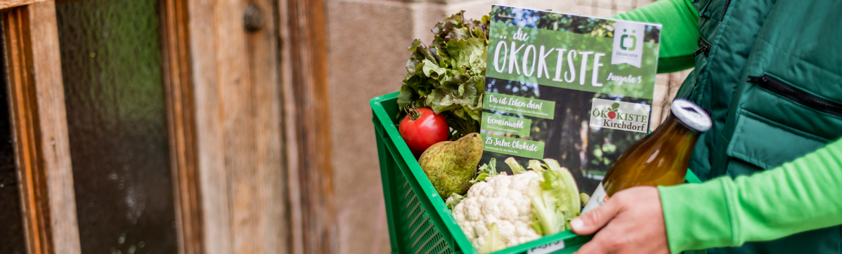 KI generiert: Eine Person hält eine grüne Kiste mit frischem Gemüse und einer Ökokiste-Broschüre.