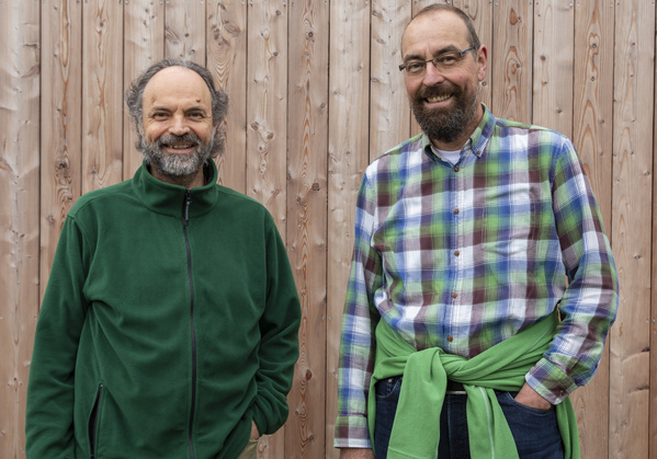 KI generiert: Zwei Männer lächeln vor einer Holzwand.