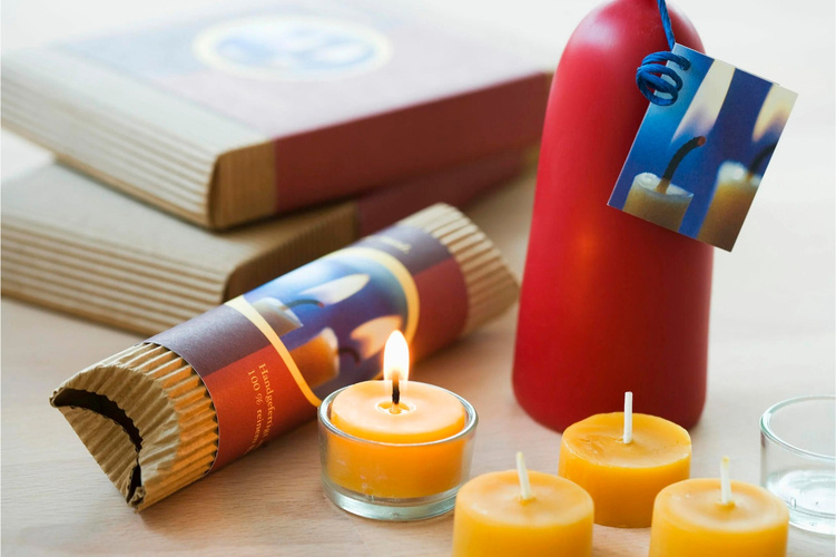 KI generiert: Verschiedene Kerzen auf einem Tisch, inklusive einer brennenden Teelichtkerze und einer roten Stumpenkerze.