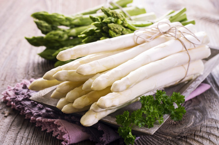 KI generiert: Frischer weißer und grüner Spargel auf Holzplatte mit Petersilie dekoriert.
