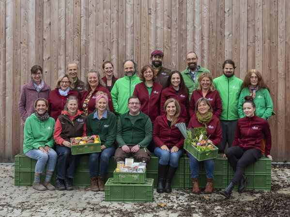 KI generiert: Eine Gruppe von Leuten posiert mit Kisten voller Gemüse und Produkten.
