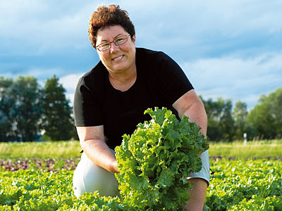 KI generiert: Eine Person hält frischen Salat auf einem Feld mit grüner Landschaft im Hintergrund.