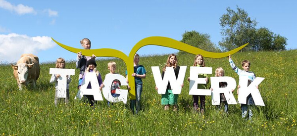 KI generiert: Kinder auf Wiese mit großen Buchstaben "TAG WERK" und einer Kuh im Hintergrund.
