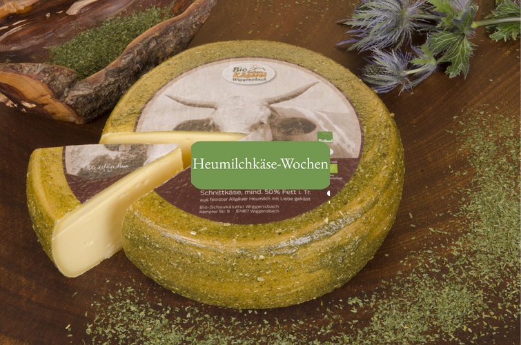 KI generiert: Ein Laib Käse auf Holzbrett, Text: "Heumilchkäse-Wochen. Schnittkäse, mind. 50% Fett i. Tr."