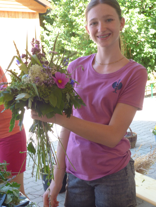 KI-generierte Beschreibung: Eine Frau hält einen Blumenstrauß in einem Gewächshaus.