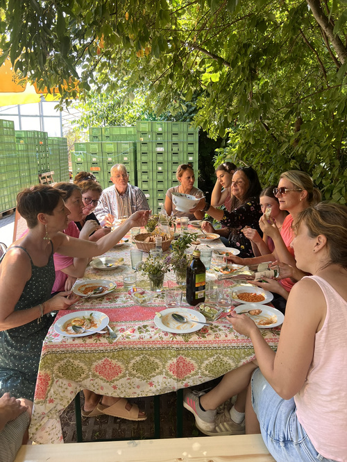 KI-generierte Beschreibung: Gruppe genießt Buffet im Freien unter Bäumen.
