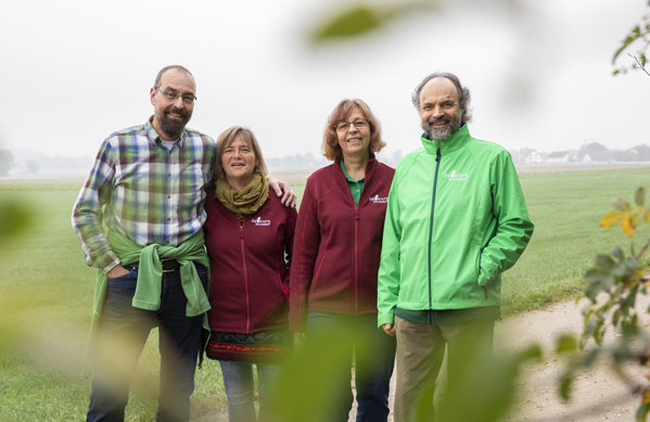 KI generiert: Vier Menschen stehen an einem Feldweg und lächeln in die Kamera.