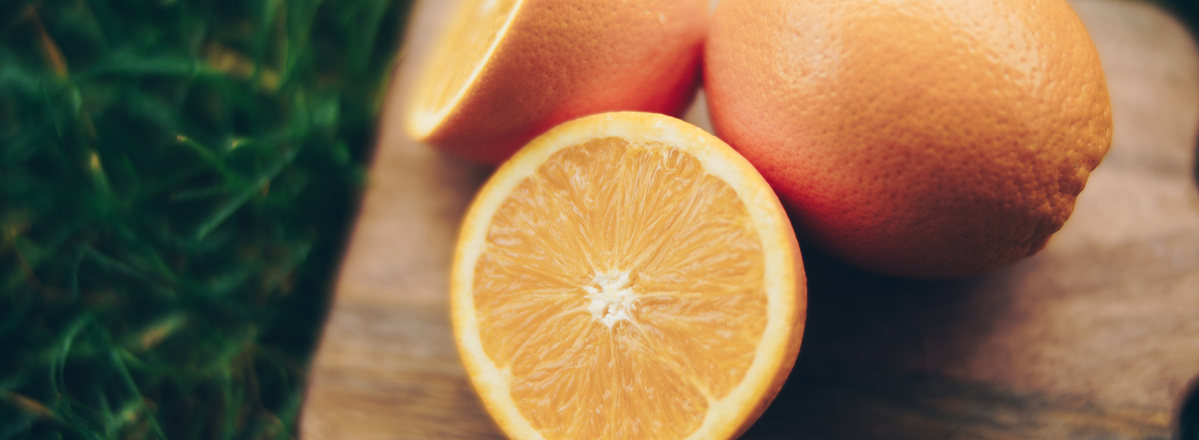 KI generiert: Das Bild zeigt eine aufgeschnittene Orange, die auf einem Holzbrett liegt, mit einem Hintergrund aus Gras. Der Fokus liegt auf der frischen, saftigen Frucht im Vordergrund.