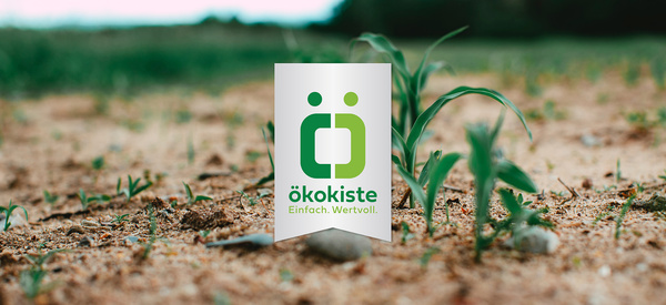 KI generiert: Ein Feld mit der Aufschrift "ökokiste Einfach. Wertvoll." über grünen Pflänzchen im Vordergrund.