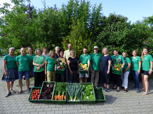 KI generiert: Eine Gruppe posiert vor einem Lieferwagen mit frischem Obst und Gemüse. Text: "oekokiste-kirchdorf.de".