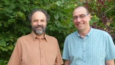 KI generiert: Ich weiß nicht, wer die Personen auf dem Bild sind. Zwei Männer stehen vor grünen Blättern.