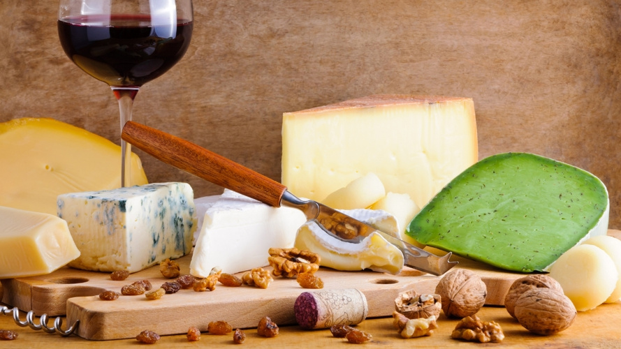 KI generiert: Käseplatte mit verschiedenen Käsesorten, einem Glas Rotwein, Nüssen und Korken auf Holzbrett.