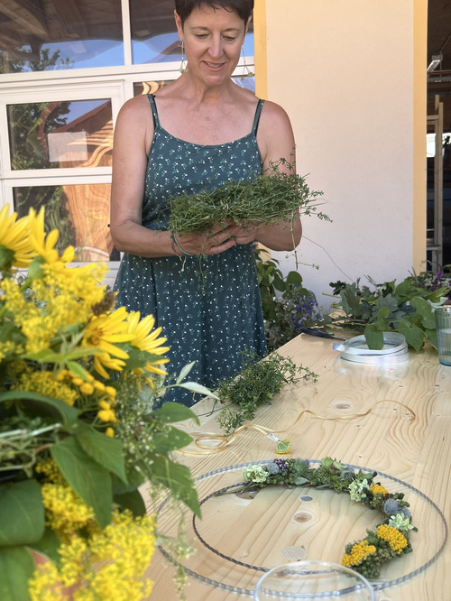 KI-generierte Beschreibung: Eine Frau präsentiert einen Blumenstrauß und einen Korb mit Gemüse.