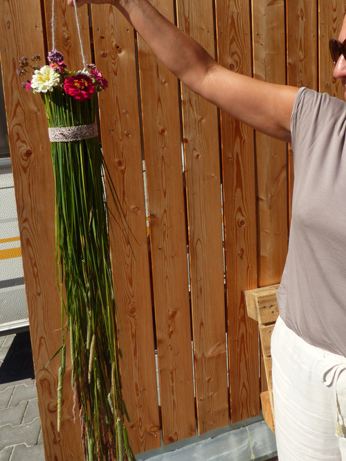 KI-generierte Beschreibung: Hauptinhalt: Person hält Blumenstrauß vor Holzwand.