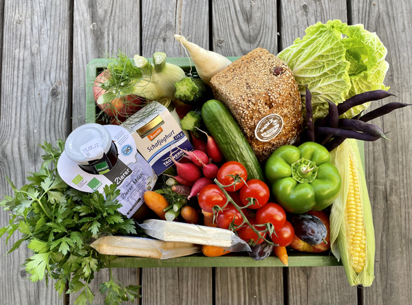 KI generiert: Eine Kiste mit frischem Gemüse, Obst, Brot und Milchprodukten auf einem Holztisch.