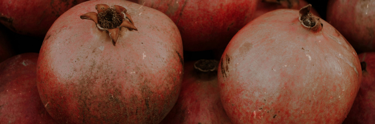 KI generiert: Das Bild zeigt eine Ansammlung von Granatäpfeln. Die Früchte haben eine rötliche Schale und liegen dicht beieinander.