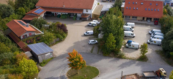 KI generiert: Luftaufnahme eines Hofs mit mehreren Gebäuden, Solarpanels und geparkten Lieferwagen.