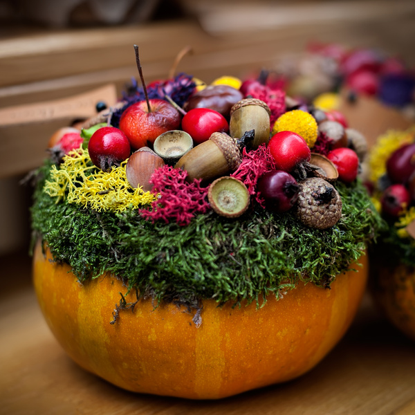 KI generiert: Herbstlich dekorierter Kürbis mit Moos, Eicheln, Beeren und buntem Blattwerk.