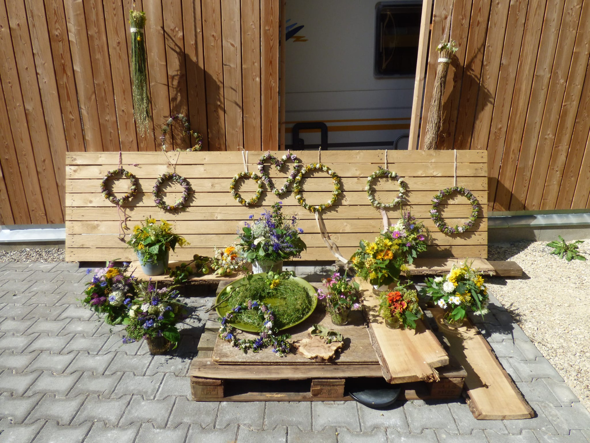 KI generiert: Blumenkränze und -arrangements sind vor einer Holzwand ausgestellt. Keine weiteren Texte vorhanden.