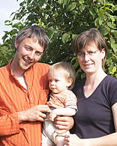 KI generiert: Ein lächelndes Paar steht mit einem Kleinkind vor einem Baum.