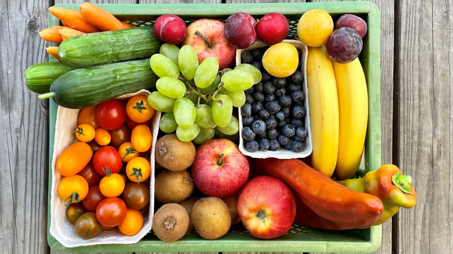 KI generiert: Eine Kiste mit frischem Obst und Gemüse, darunter Tomaten, Gurken, Trauben, Äpfel, Bananen und Pflaumen.