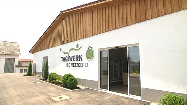 KI generiert: Gebäude einer Bio-Metzgerei mit dem Schriftzug "TAGWERK BIO METZGEREI" auf der Außenwand.